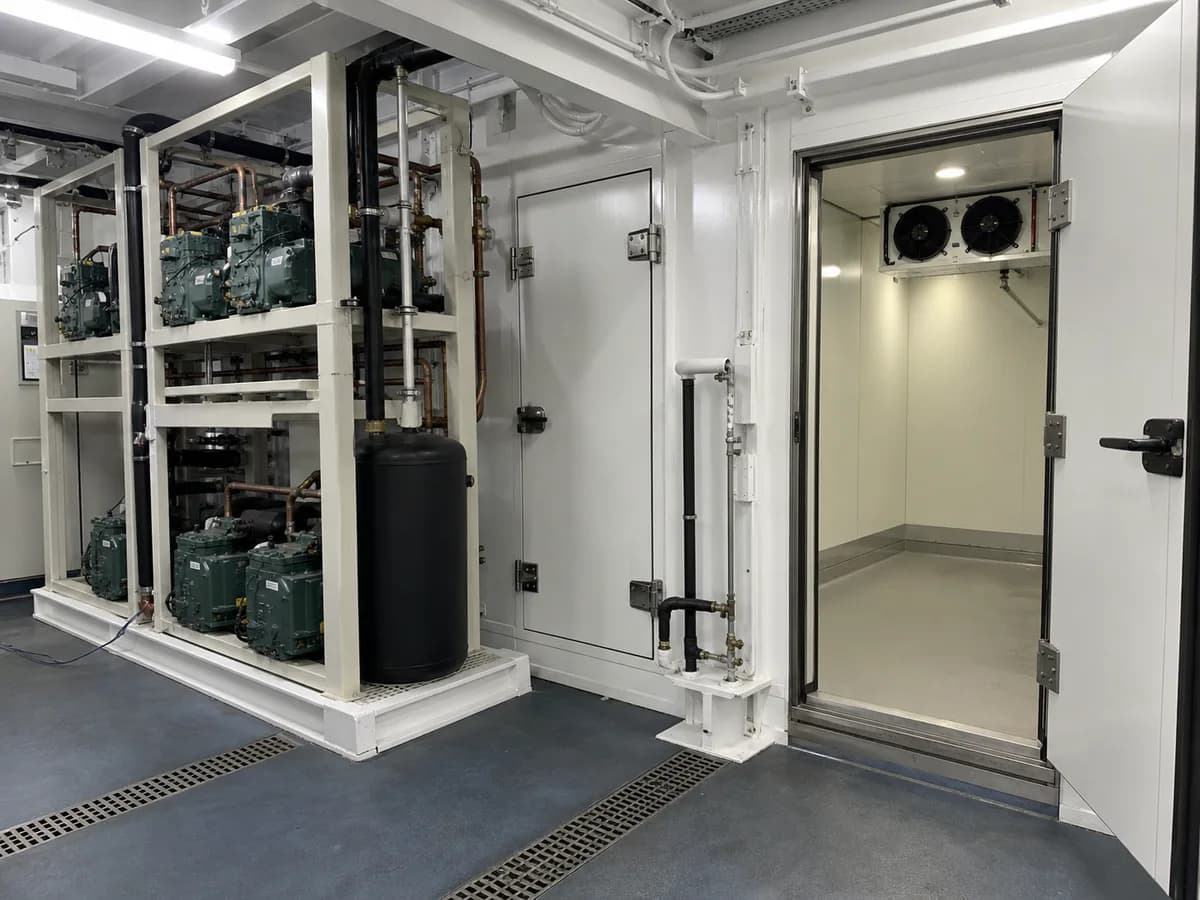 Unbranded marine provision refrigeration plant beside an insulated shipboard cold-room doorway and air cooler